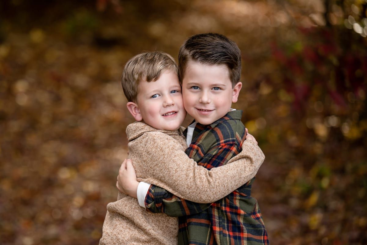 Two young brothers hugging in front of autumn leaves